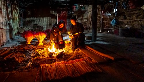 Free Two people crafting incense sticks by a warm fire inside a rustic setting. Stock Photo