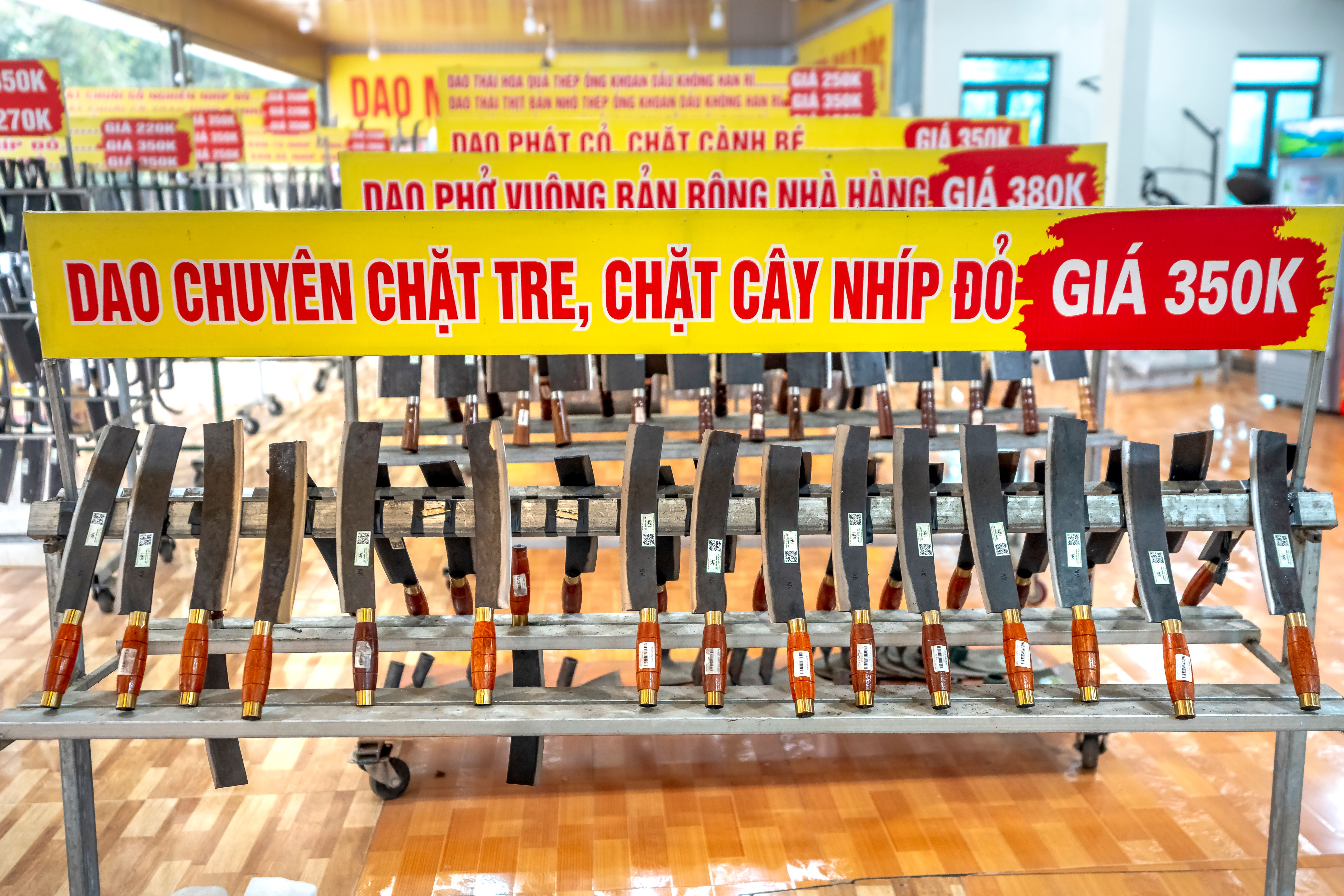 A shop display of traditional Vietnamese cleavers with wooden handles, labeled in Vietnamese.
