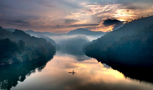 Free Peaceful sunrise view over a misty river and mountains, featuring a lone kayaker. Stock Photo