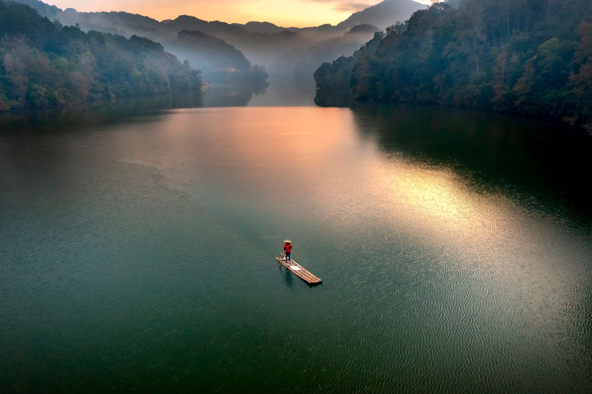 A serene scene of a lone person paddling a raft on a misty lake at sunrise with surrounding hills.