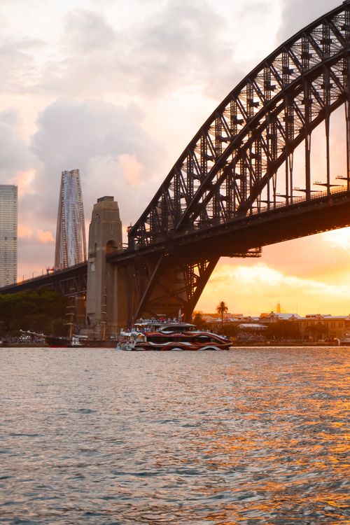 Free Scenic sunset view of the Sydney Harbour Bridge with boats and city skyline. Stock Photo