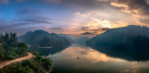 Free A breathtaking view of a peaceful lake surrounded by lush hills during a vibrant sunset. Stock Photo