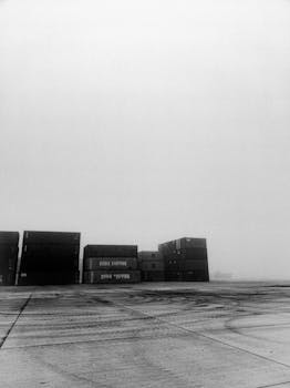 A misty black and white image of cargo containers creating a moody atmosphere in an open field.