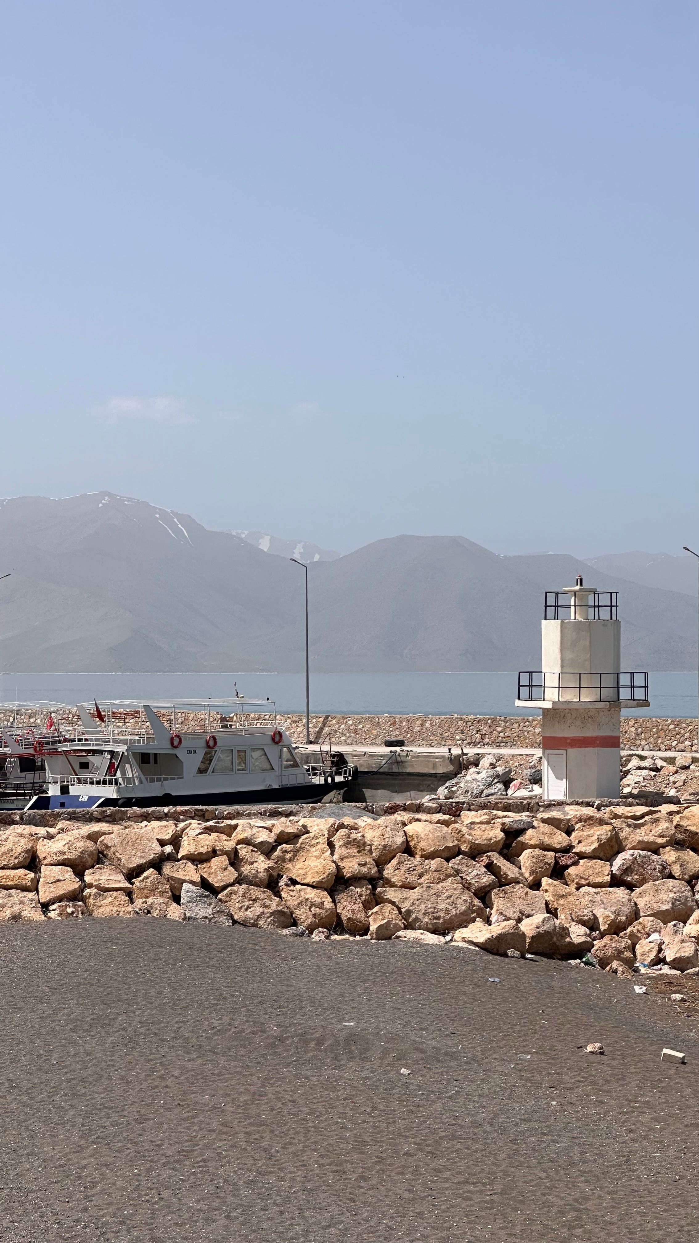 Lighthouse at a serene lakeside with rocky shoreline and distant mountains.