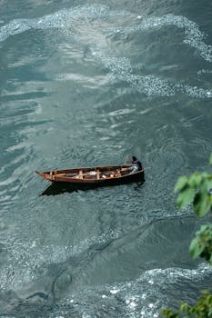 A person rows a wooden boat on a calm, green river, viewed from above.