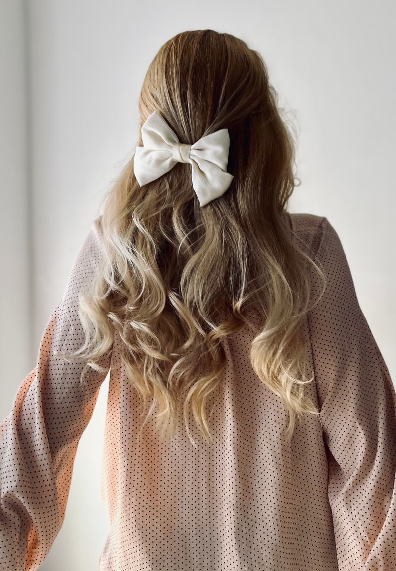 Woman with long blonde hair tied with a white bow, back view