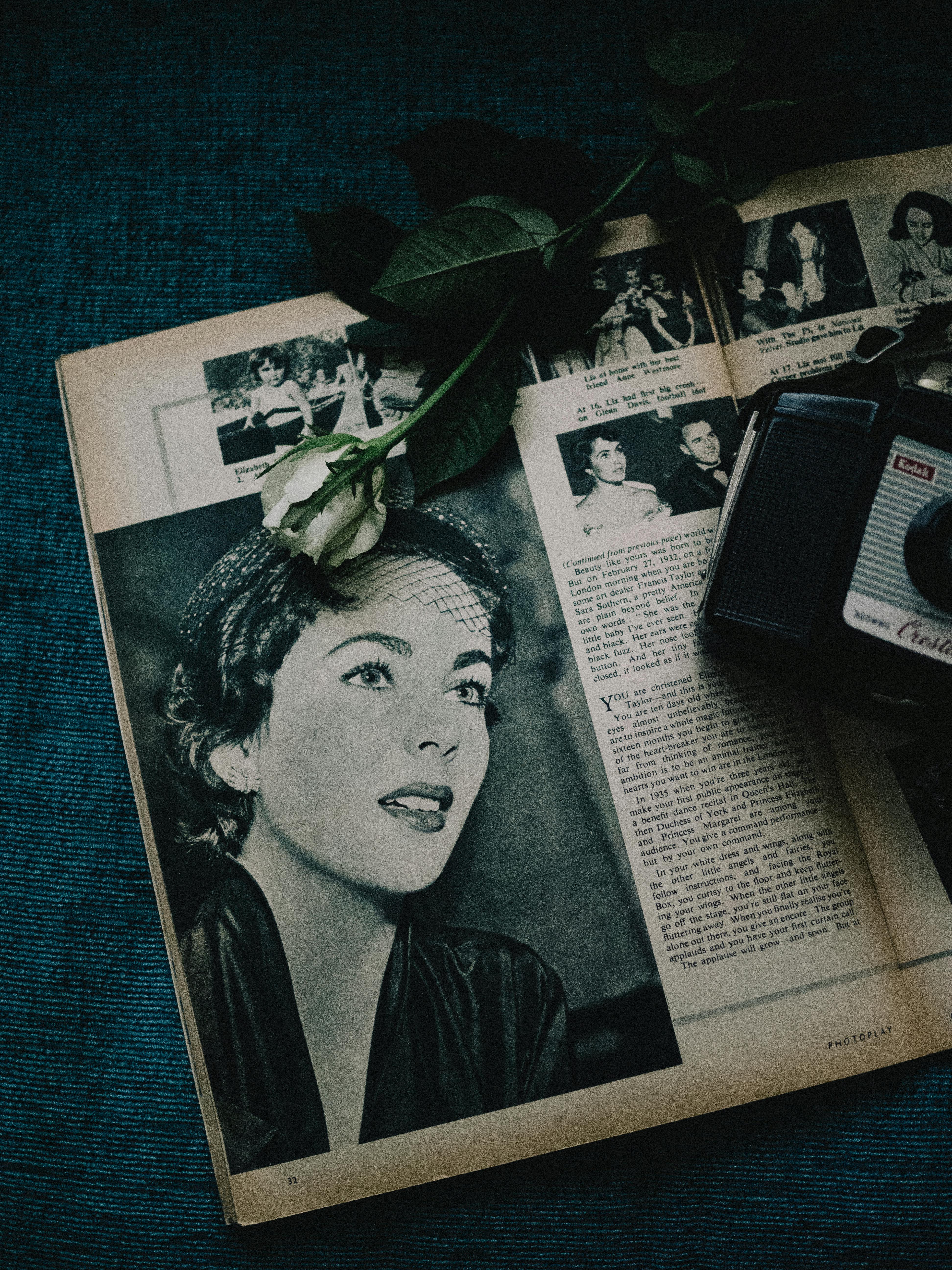 A vintage magazine and retro camera with a white rose set on a dark fabric background, evoking nostalgia.