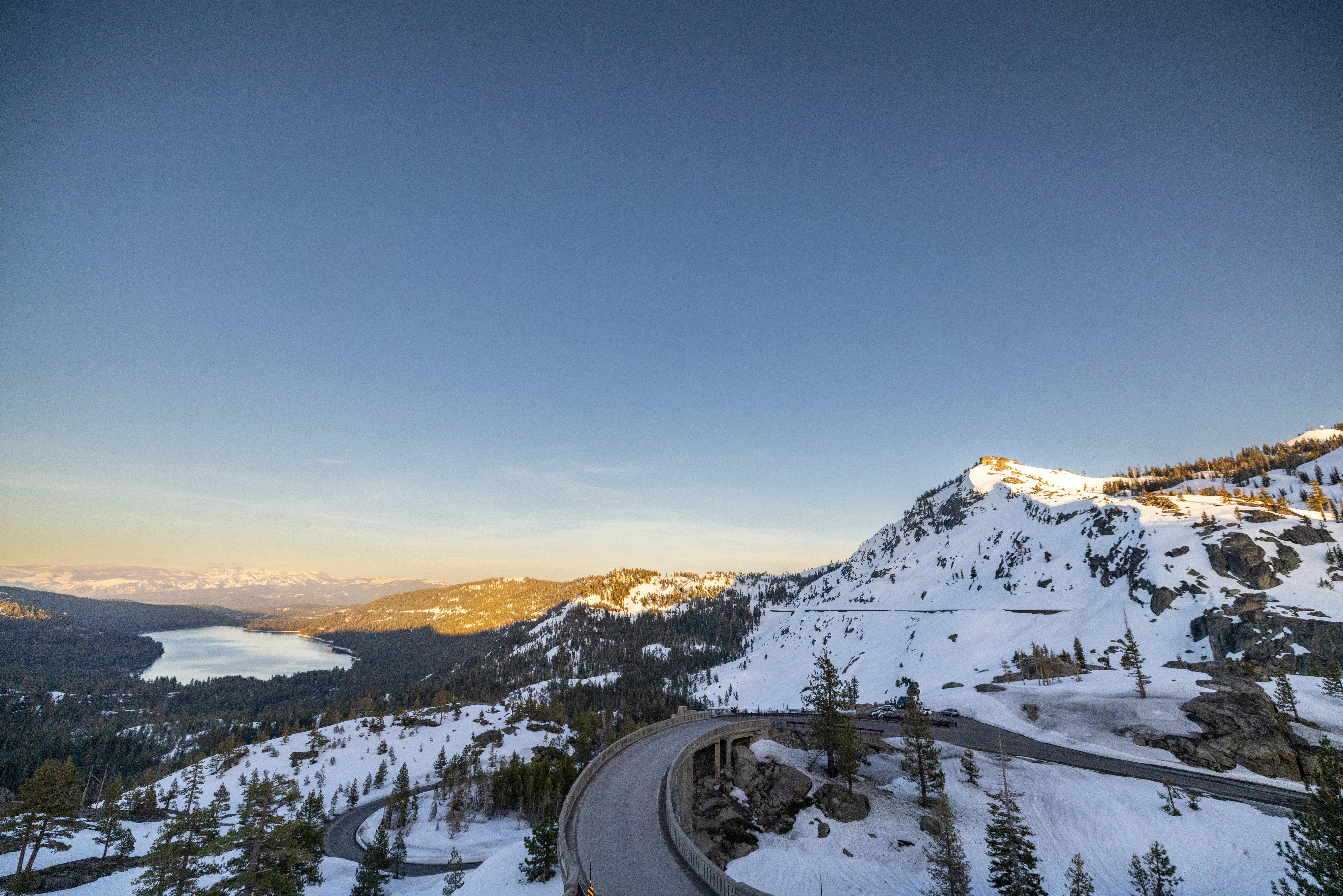 A breathtaking winter landscape at Donner Pass showcasing snow-covered mountains and a serene lake under a clear sky.