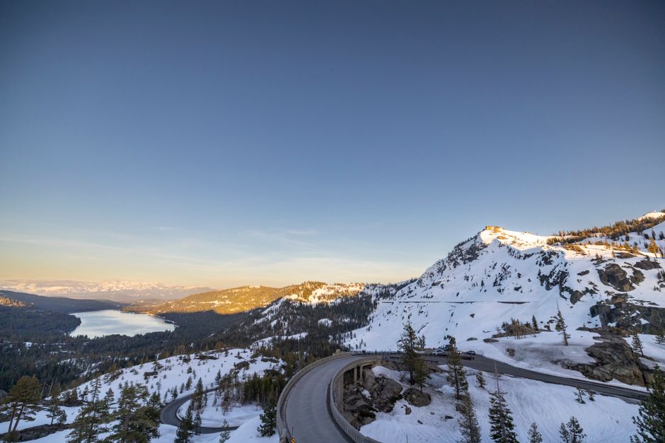 A breathtaking winter landscape at Donner Pass showcasing snow-covered mountains and a serene lake under a clear sky.