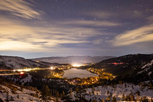 A breathtaking night vista of Donner Lake surrounded by snowcapped mountains and a starlit sky.