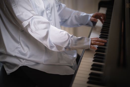 Close-up of a person playing piano, focusing on hands and white shirt.