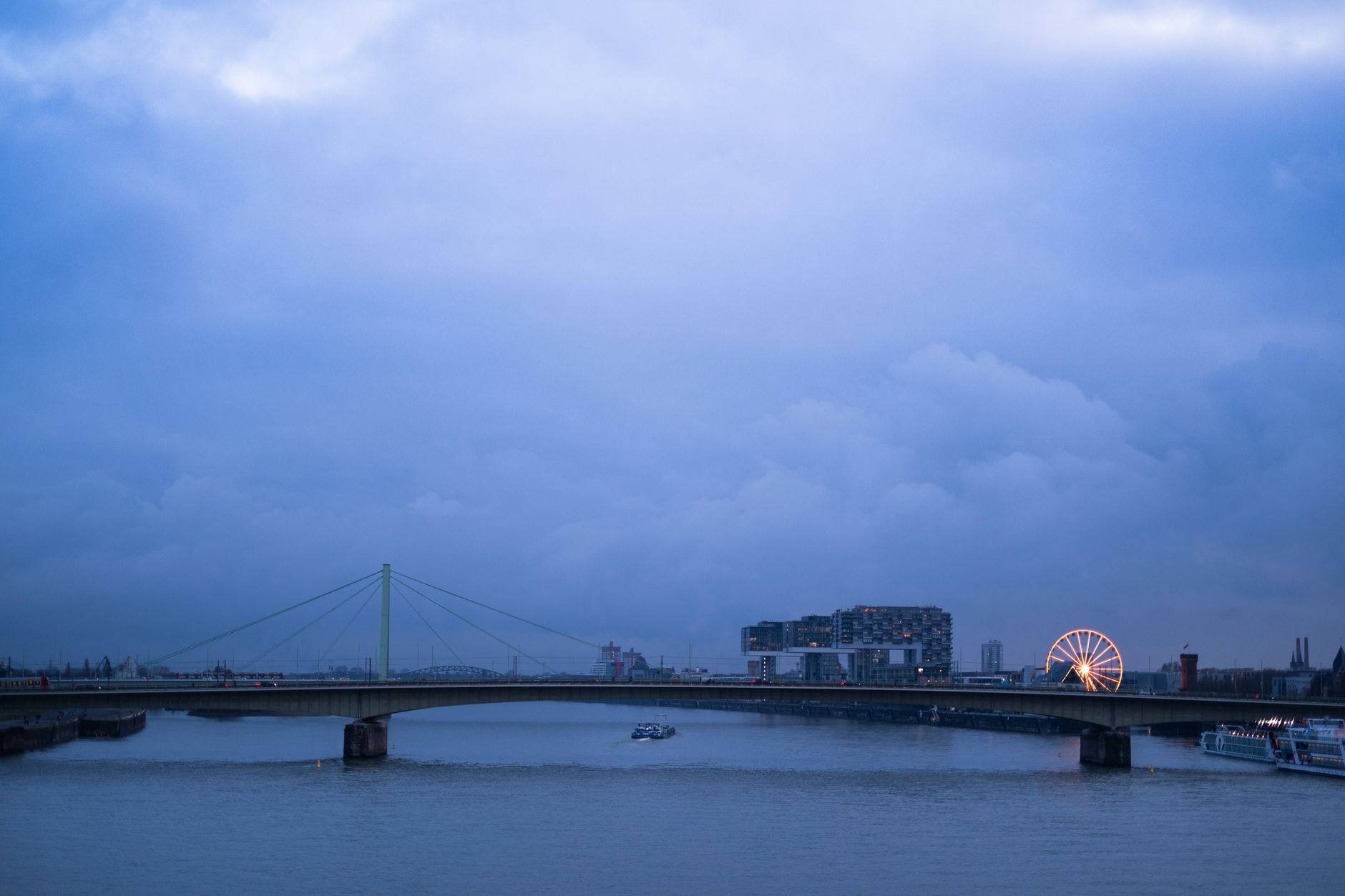 Twilight view of a bridge and illuminated ferris wheel against cloudy sky in Cologne, Germany.