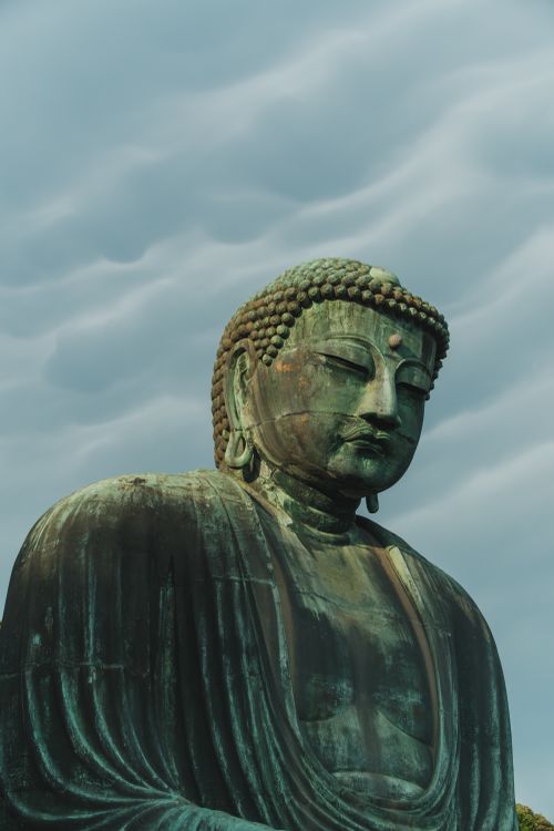 Free The bronze Great Buddha statue in Kamakura, Japan, set against a dramatic cloudy sky, showcases serene majesty. Stock Photo