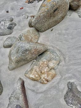 Close-up of textured rocks partially buried in soft beach sand.