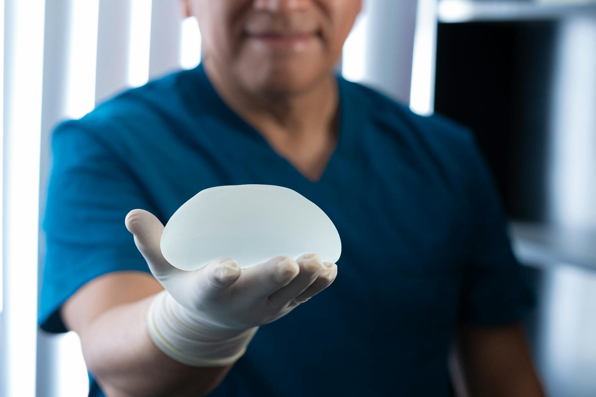 Plastic surgeon presenting a silicone breast implant in a medical setting.