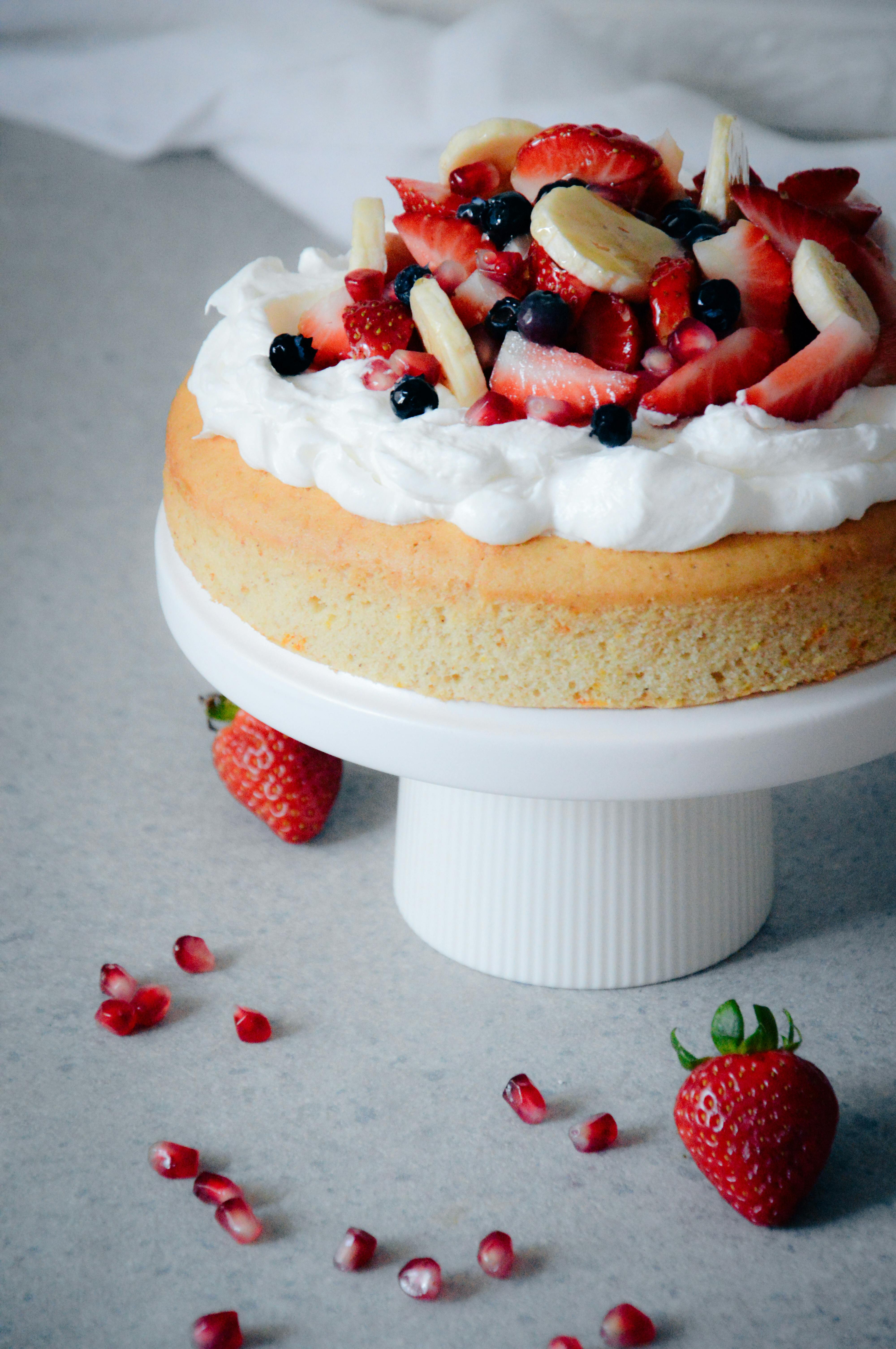Mouthwatering sponge cake with fresh fruit and cream on a white stand.