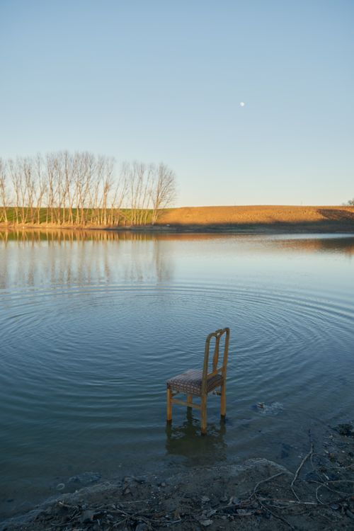 Free A single chair in a tranquil lake setting reflects solitude under the evening sky. Stock Photo