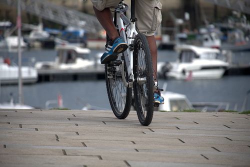 Free A cyclist pedals along a waterfront boardwalk near a marina filled with boats. Stock Photo