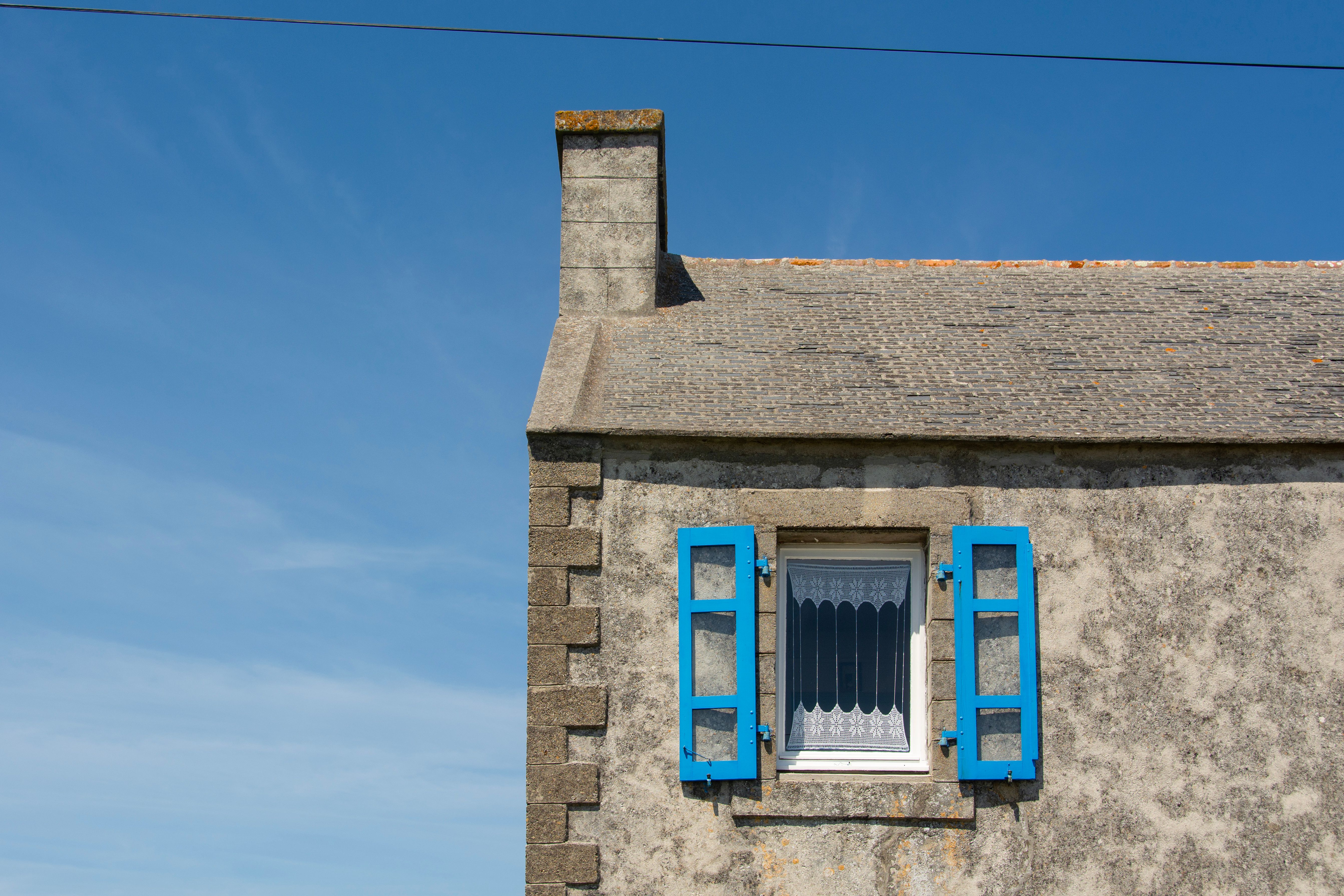 Charming stone house with blue shuttered window against clear sky in Bretagne, France.