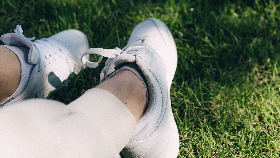 Person relaxing on grass wearing casual white sneakers, exuding a laid-back and serene vibe.
