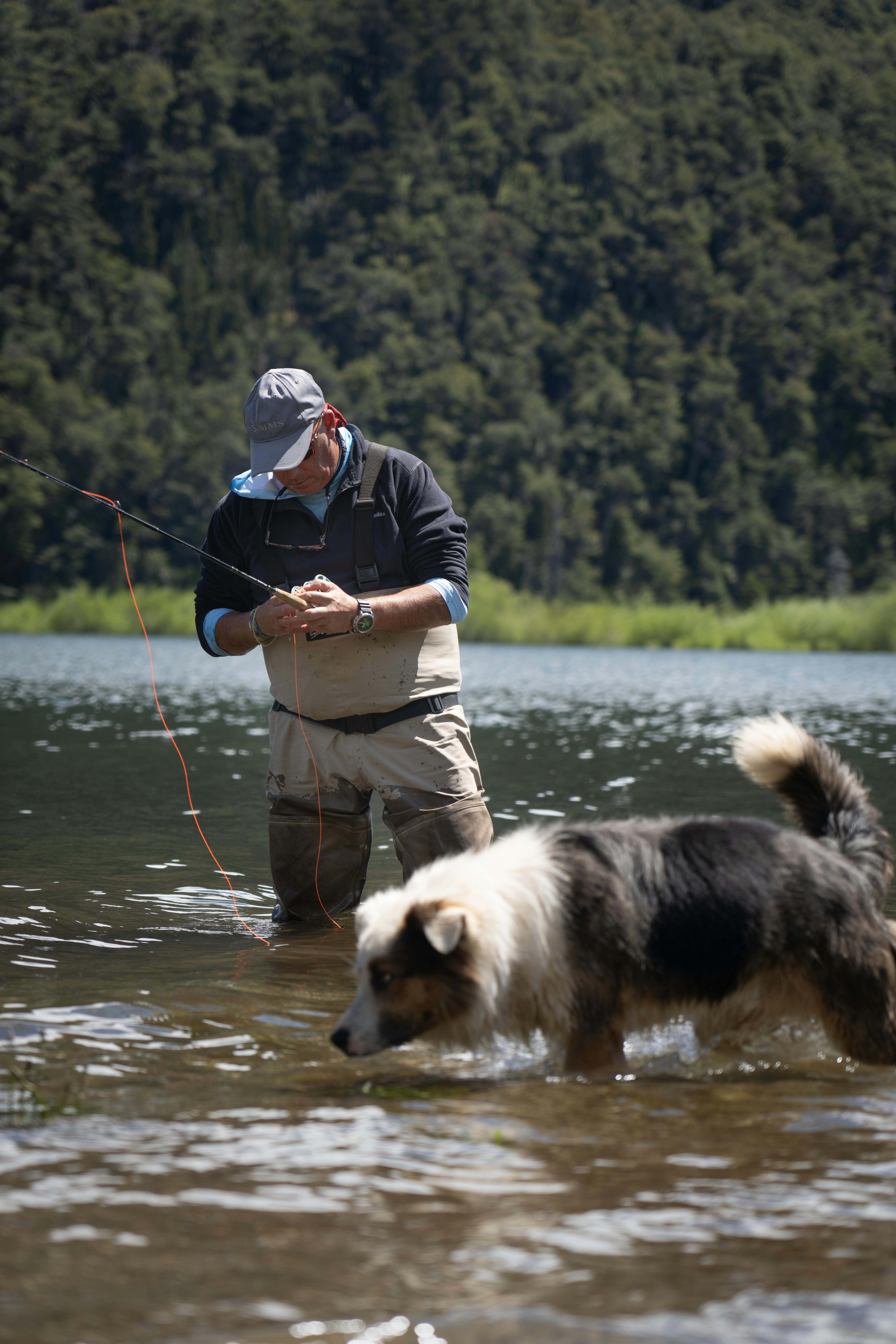 Man fly fishing with a dog in a serene Argentine lake setting, surrounded by nature.