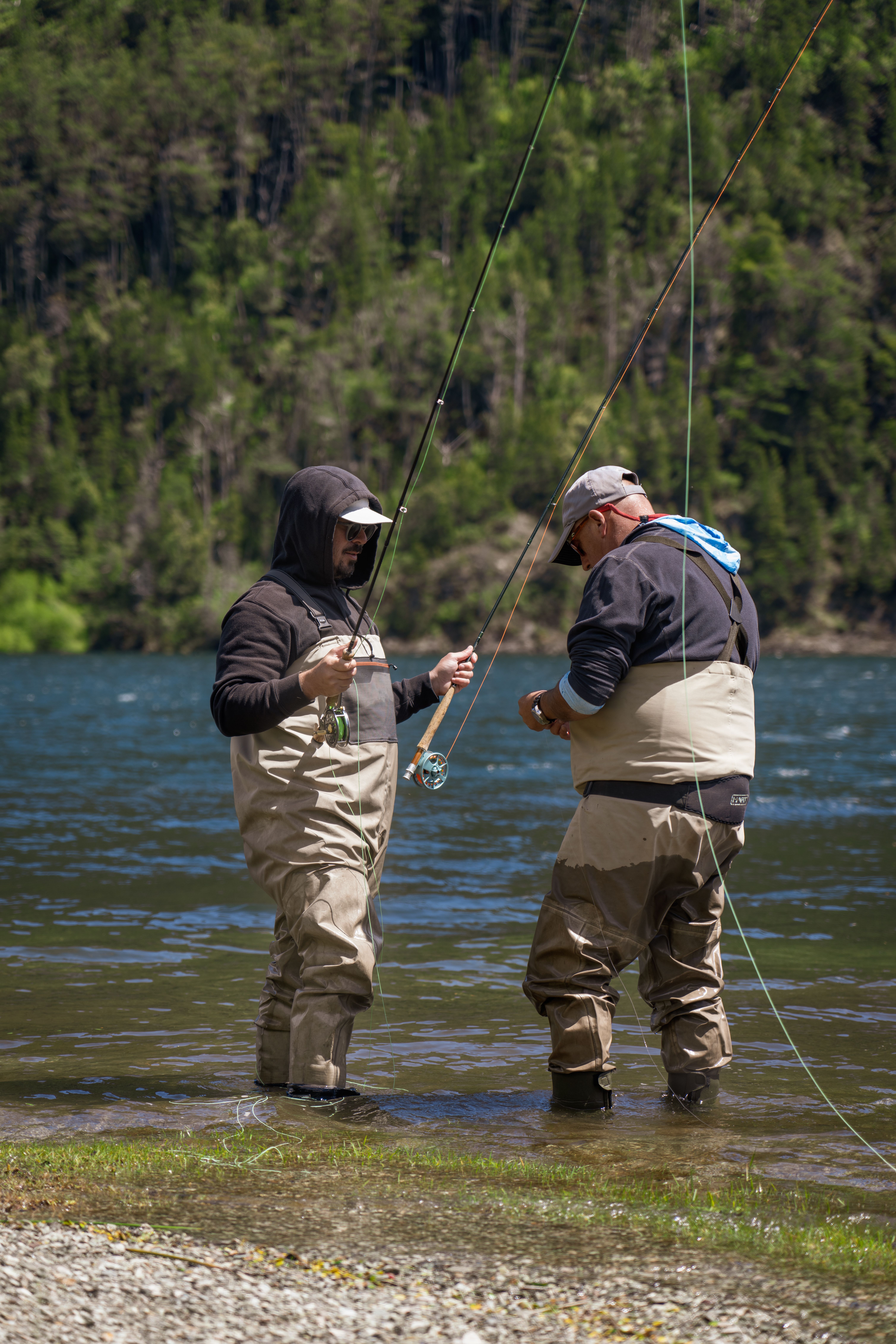 Two men fly fishing in a scenic Patagonian lake, surrounded by lush forests.