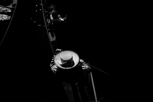 Artistic black and white image of a gondolier at night in Venice, capturing the serene canal atmosphere.
