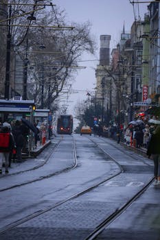 Rainy day on a bustling Istanbul street with tram and people under umbrellas.