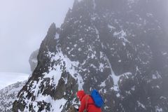 A person dressed in red scaling a rugged, snow-covered ridge against jagged peaks in Zermatt.