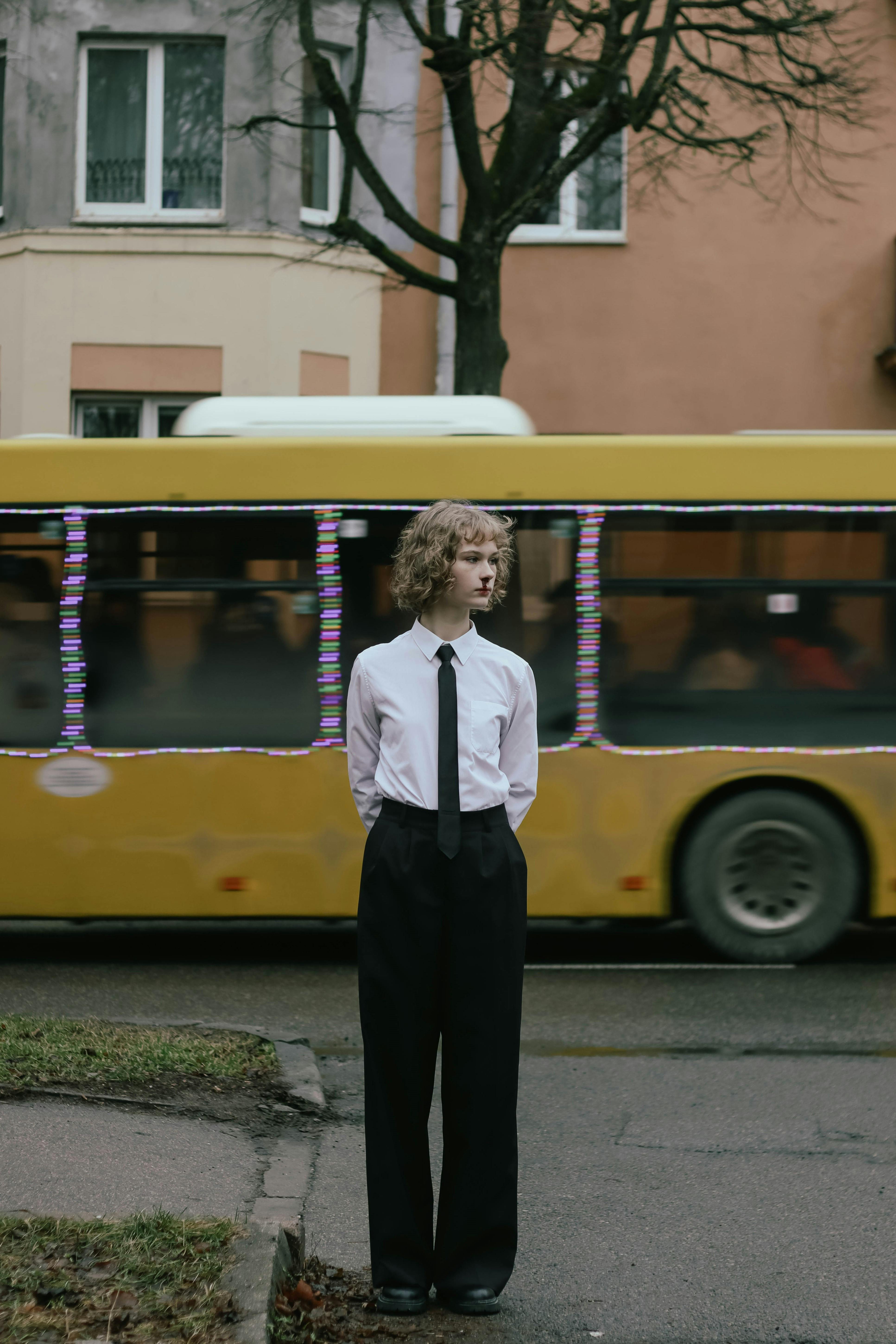 A young adult in formal attire standing in front of a yellow bus in Minsk, Belarus.