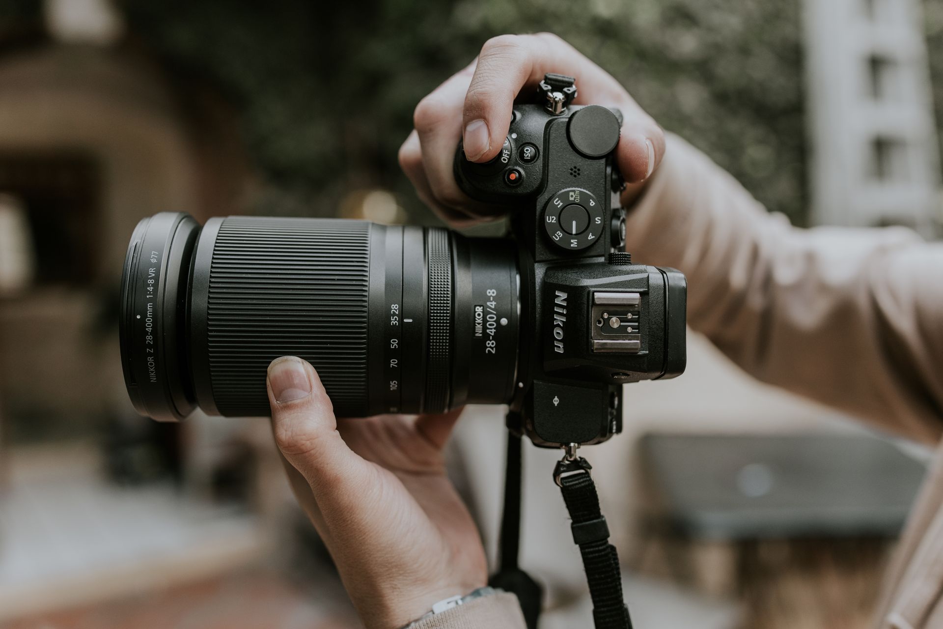 Close-up of hands holding a DSLR camera with telephoto lens outdoors.