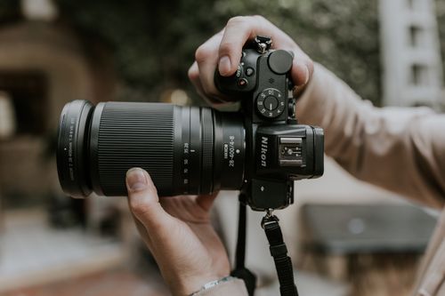 Free Close-up of hands holding a DSLR camera with telephoto lens outdoors. Stock Photo