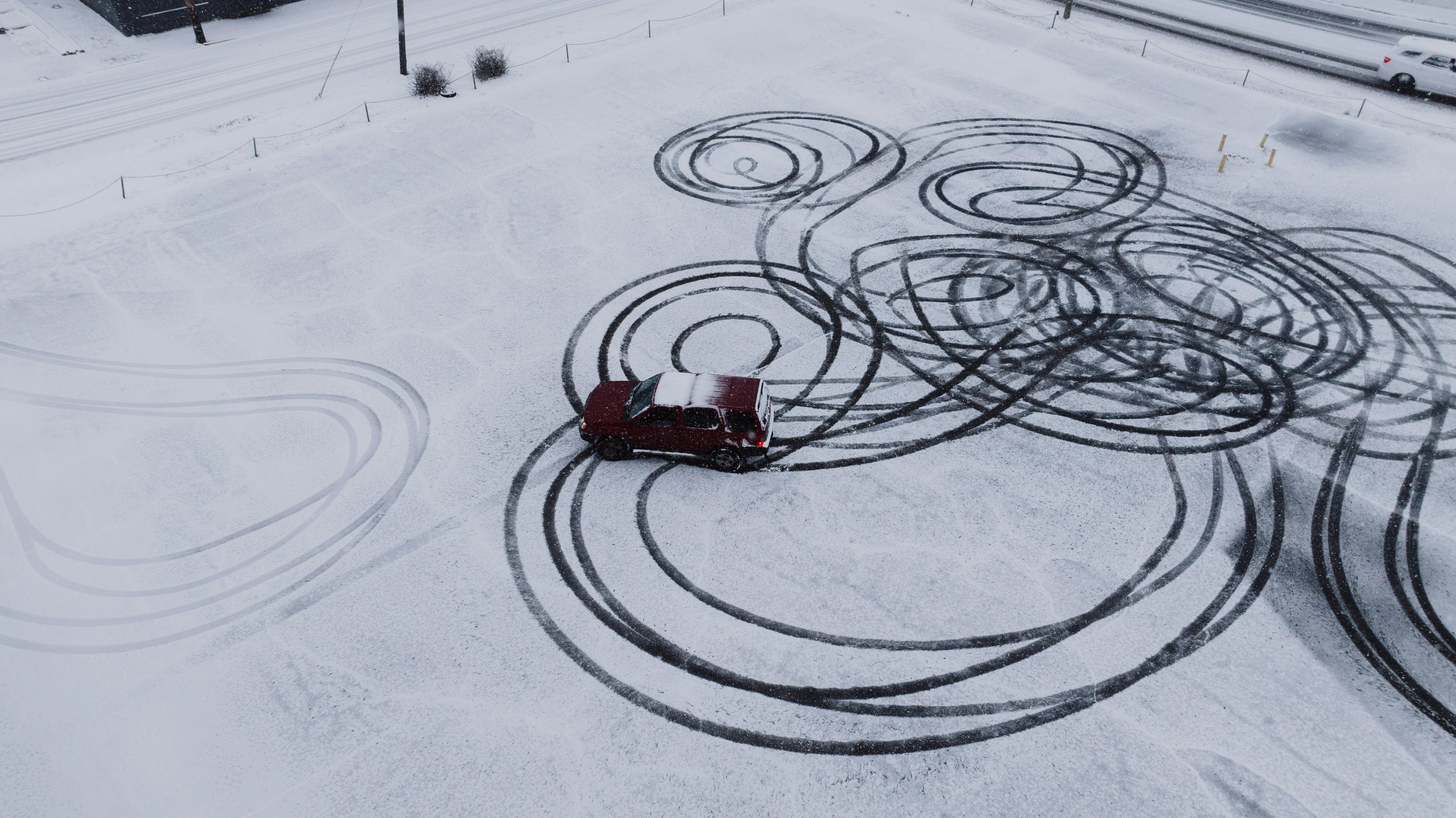 Samochód z napędem na tylne koła driftujący na zaśnieżonej drodze, z widocznymi śladami poślizgu.