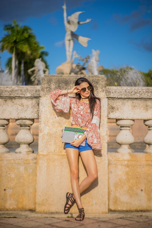 Mujer Vestida Con Blusa Roja Y Pantalones Cortos Azul Apoyado En La Pared