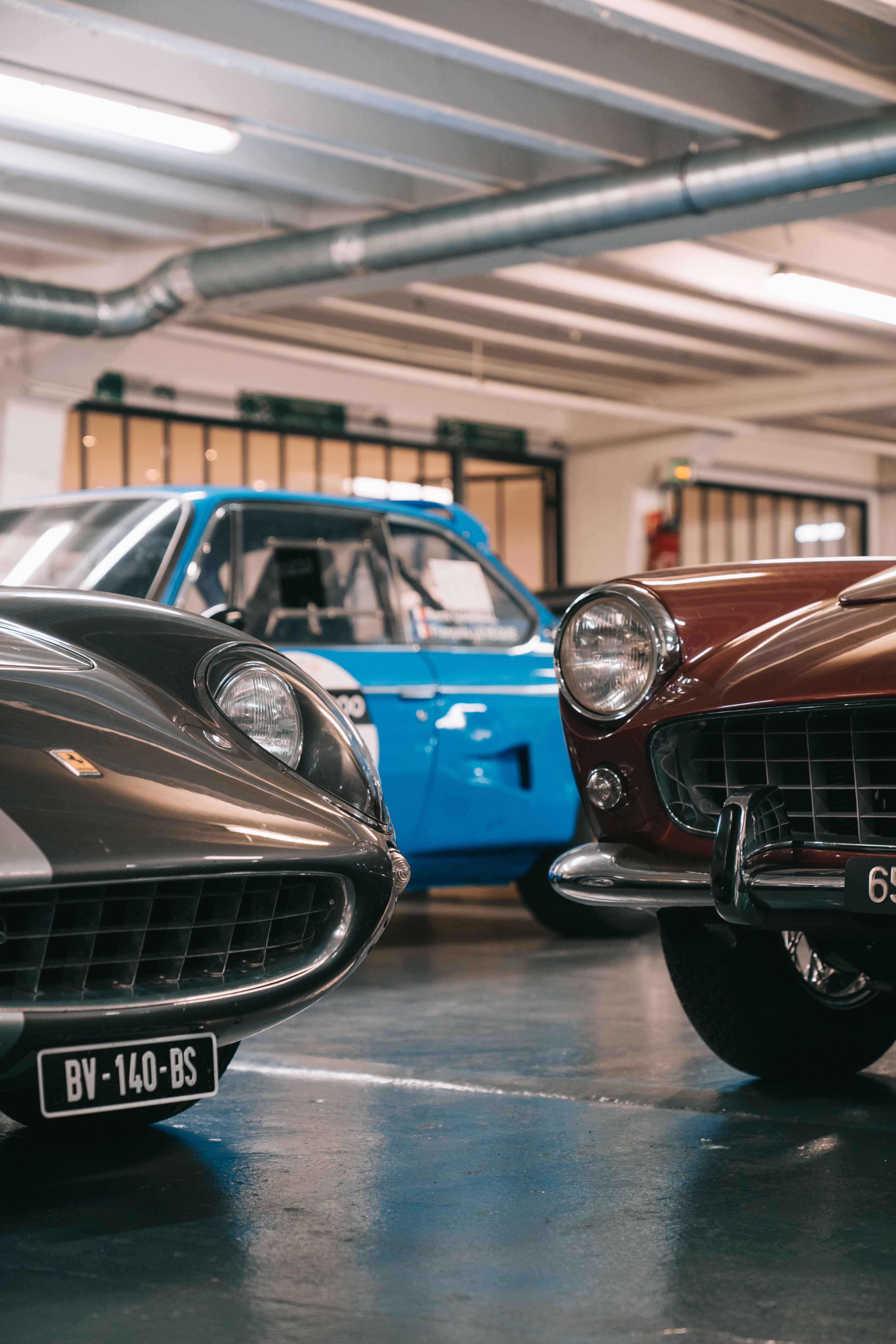 Close-up view of classic vintage sports cars displayed in an indoor garage, showcasing elegance.