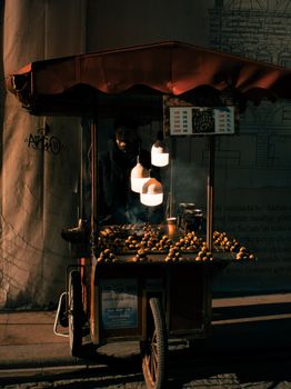 Atmospheric scene of a street vendor selling roasted chestnuts at night.
