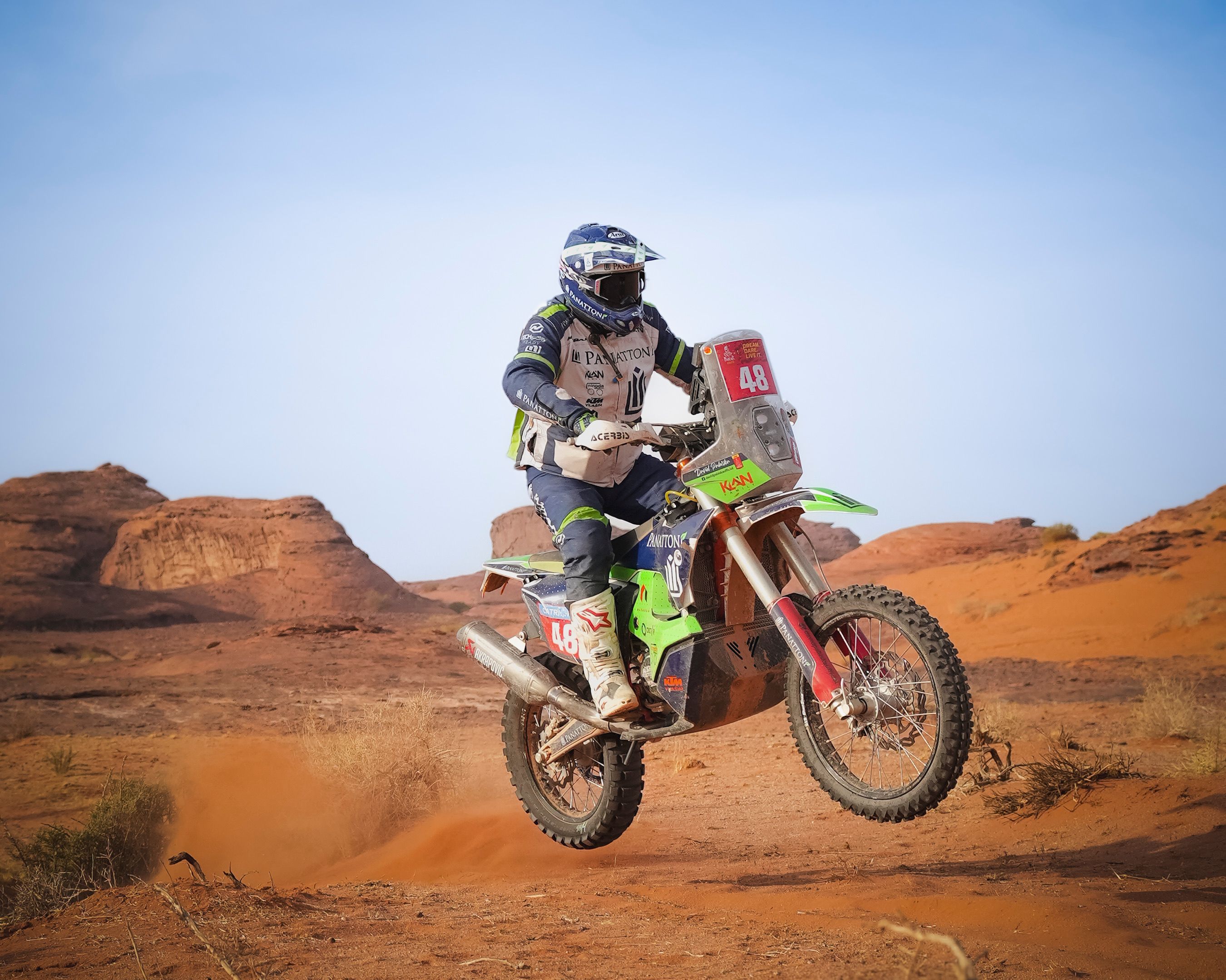Motorcycle racer jumping in arid desert landscape, showcasing speed and adventure.