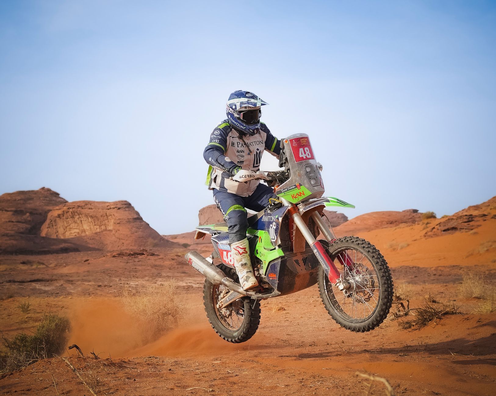 Motorcycle racer jumping in arid desert landscape, showcasing speed and adventure.
