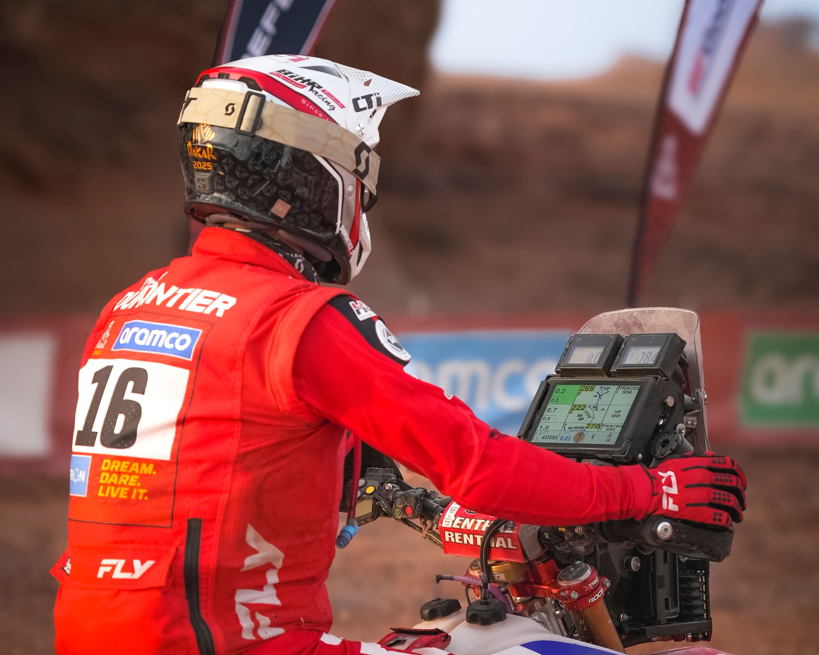 Motorcyclist in red gear navigating desert rally with GPS.