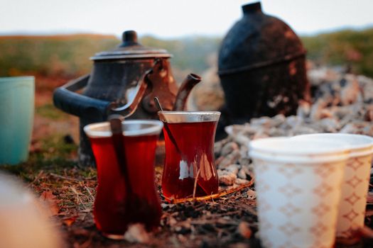 Traditional tea brewing outdoors with teapots and glasses by the campfire.