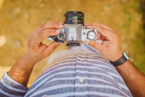 Free A man holding a vintage camera outdoors, focusing on the device for travel or leisure photography. Stock Photo