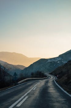 Curved mountain road leading into a serene landscape at sunrise, offering a peaceful journey.