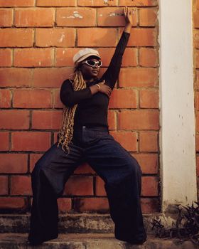 Stylish woman in casual fashion posing confidently against a brick wall.