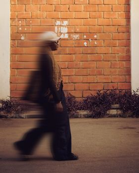 A blurred motion capture of a woman walking along a brick wall, conveying movement.