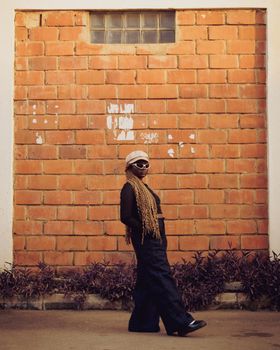Fashionable woman poses confidently against a brick wall.