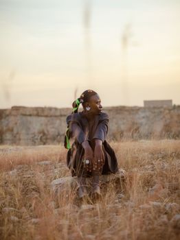 An adult woman sitting in a dry field during sunset, exuding serenity and introspection.