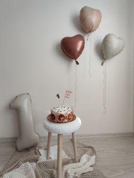 Stylish first birthday setup with cake and heart-shaped balloons indoors.