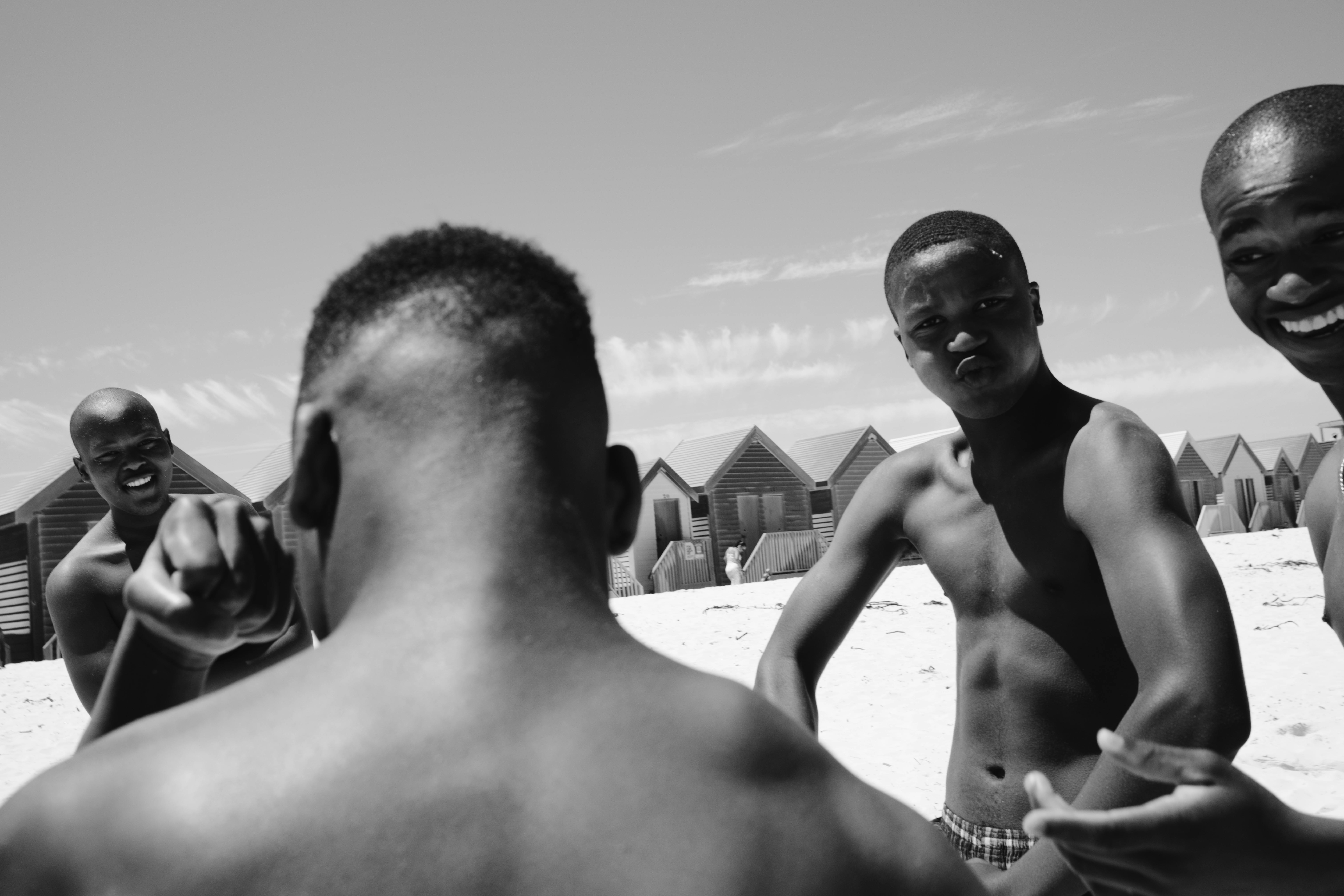 Black and white image of friends interacting near colorful beach huts on a sunny day.