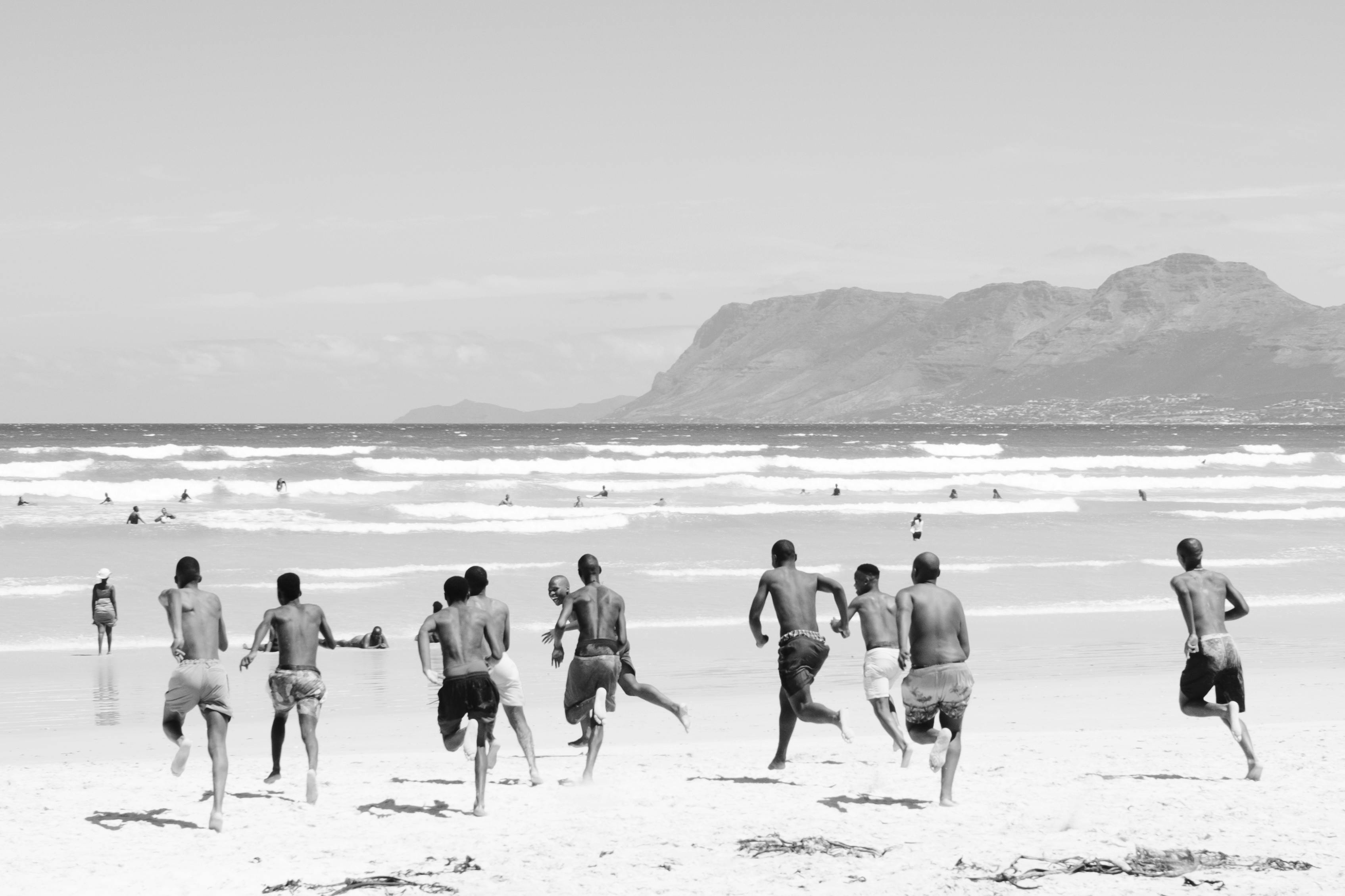 A group of boys runs joyfully towards the ocean waves on a sunny beach day.