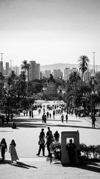 Black and white photo of a city park with a monument and people walking.